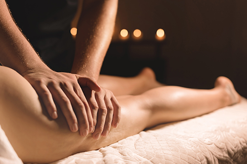 A masseur in a dark room does a hip massage with oil for a woman. Spa procedures massage women