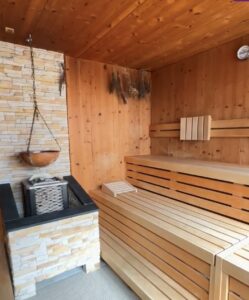 Holzverkleidete Sauna mit Steinofen und getrockneten Kräutern an der Wand