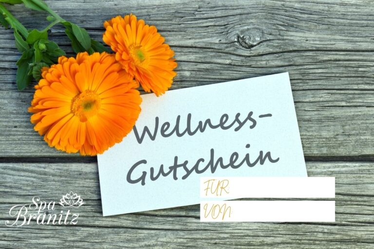 Zwei orange Ringelblumen und eine Karte mit dem Text Wellness-Gutschein auf Holz