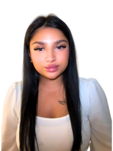 Junge Frau mit langen schwarzen Haaren, neutralem Blick und weißer Bluse vor Weiß